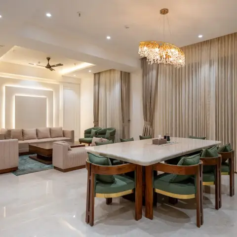 Open-plan dining zone with a thick white marble table and eight bottle-green teak armchairs under a linear crystal chandelier