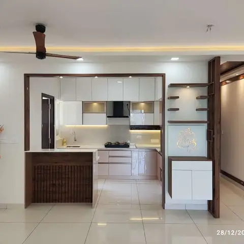 Open-plan entry hallway with a pink-and-white L-shaped kitchen on the left and a backlit pooja niche with dark wood frame on the right
