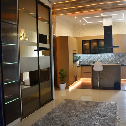 Open-plan entry with a navy and gold LED-lit sliding-door wardrobe unit opening onto a kitchen with hexagonal-tile backsplash and a living seating area beyond