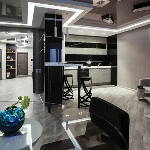 Open-plan flat in black gloss and grey where a bar counter with two scroll-legged stools splits the kitchen from the lounge