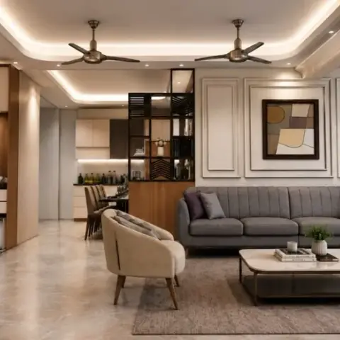 Open-plan flat where a grey channel-back sofa sits against a moulded panel wall under twin fans, with a marble-top coffee table on a jute rug