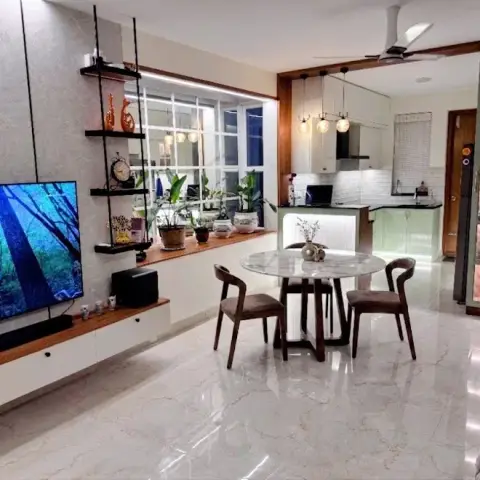 Open-plan floor seen end to end: a grey stone-clad TV wall with black metal floating shelves, a round marble-top dining table in the middle