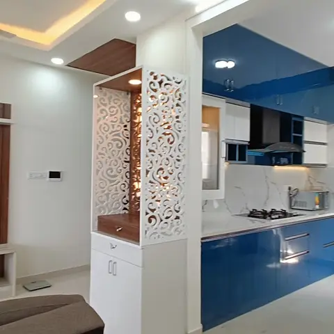 Open-plan frame showing a living room with a wood-and-marble TV unit and a glossy blue modular kitchen side by side
