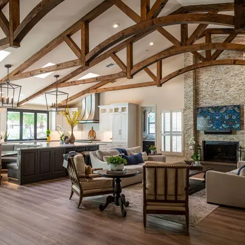 Open-plan great room with a curved wood-truss vaulted ceiling, stacked-stone fireplace, and adjoining kitchen island and dining nook.