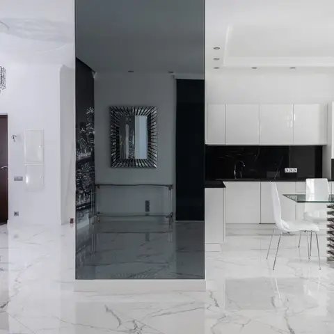 Open-plan home in black and white with a mirrored partition column dividing the entrance hall from a glossy white kitchen and a glass-top dining table on a