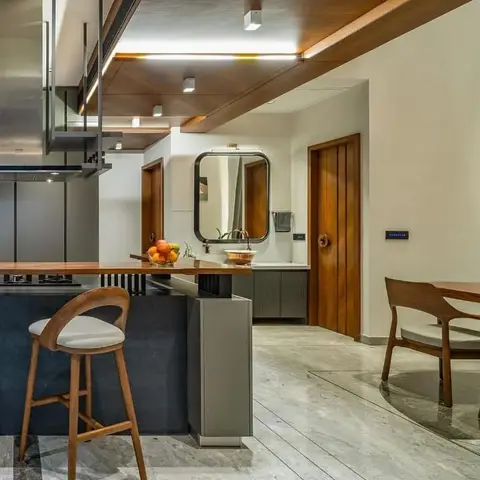 Open-plan home interior with a wood-topped kitchen island and bar stools in the foreground, a round mirror over a wash counter
