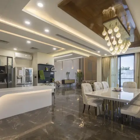 Open-plan home viewed from the kitchen island past a marble dining table under a cascading glass-bead chandelier toward the living room