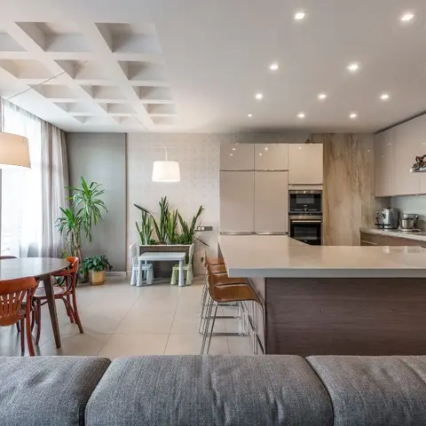 Open-plan home with a coffered waffle-pattern false ceiling, a round wood dining table, and a white kitchen island with bar seating all visible together.