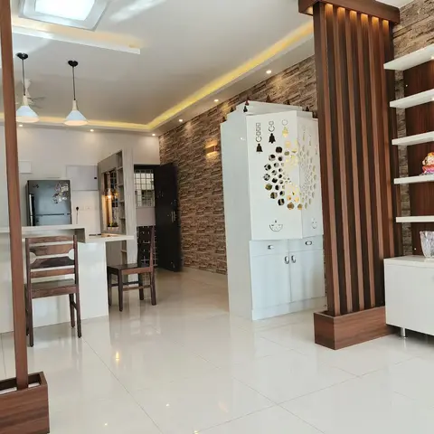 Open-plan home with a fluted wood-and-stone-clad partition dividing a kitchen and dining pass-through from a white jaali-cut pooja unit and a walnut open-shelf