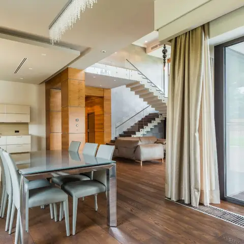 Open-plan home with a glass dining table off the kitchen, a floating staircase and leather sofa in the living area beyond