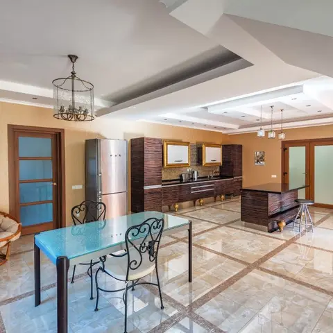 Open-plan kitchen and dining area with dark wood cabinetry, gold-framed mirror accents, and a diamond-patterned marble floor.