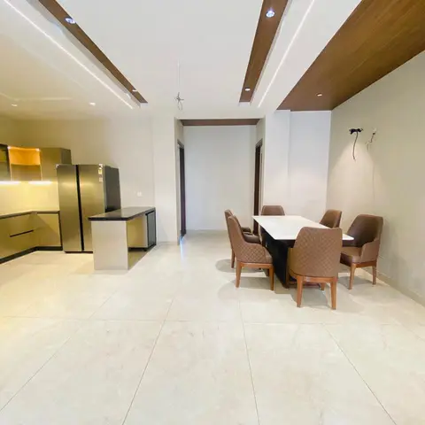 Open-plan kitchen and dining space with olive-gold gloss kitchen cabinetry, a wood-clad ceiling strip with profile lighting over the dining table