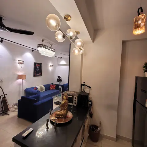 Open-plan kitchen counter and living room with a navy velvet chesterfield sofa, a globe-bubble chandelier and eclectic brass decor.