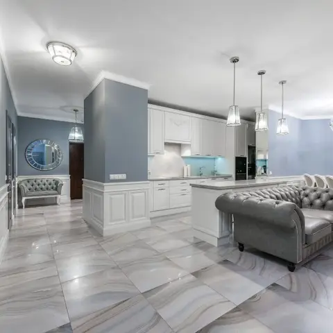 Open-plan kitchen, dining and entry with blue-grey wainscoted walls, a white shaker kitchen island under glass pendant lights, a tufted grey chesterfield sofa
