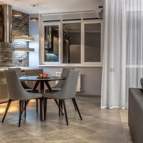 Open-plan kitchen-dining-living space with an exposed brick-look backsplash wall, cluster pendant lighting over a round dining table with grey upholstered