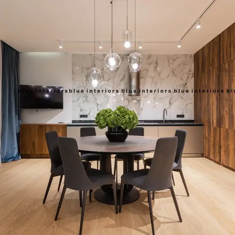 Open-plan kitchen-dining-living space with a round dark-stone dining table for six grey upholstered chairs, three globe glass pendants