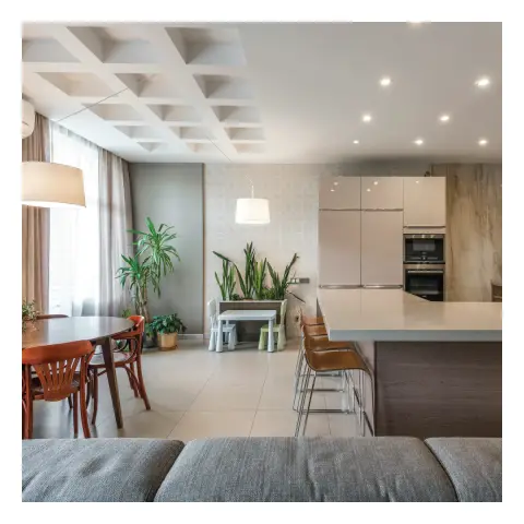 Open-plan kitchen-dining shot over the back of a grey sofa: a pale quartz island with three bentwood bar stools