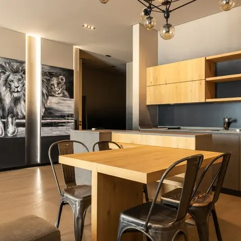 Open-plan kitchen-dining space with a wood block table and industrial metal chairs facing a dark handleless kitchen with open wood shelving