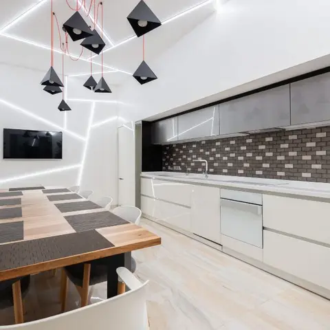 Open-plan kitchen-dining space with a handleless white kitchen run, brick-pattern mosaic backsplash, angular black pendant lights on red cords