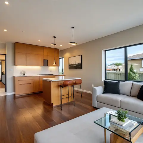 Open-plan kitchen island with two black cone pendants flowing into a grey sofa living area beside black-framed windows.