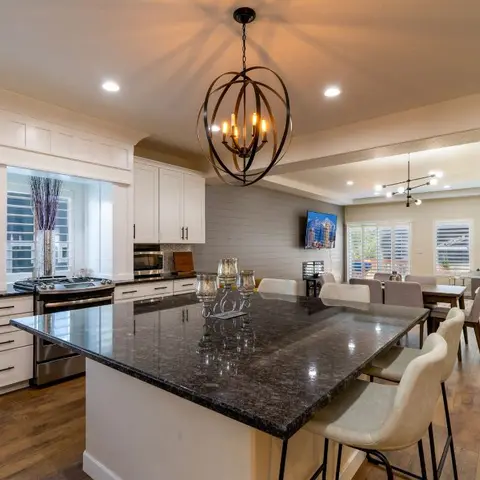 Open-plan kitchen with a black granite waterfall island and orb chandelier flowing into a dining table and a sectional-sofa living area beyond.