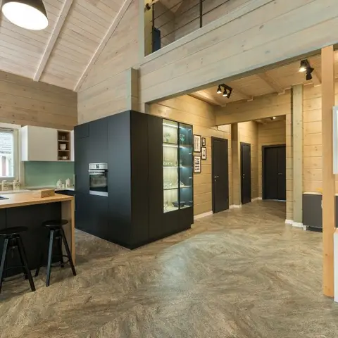Open-plan kitchen with a matte black island and glass-front display cabinet beneath a vaulted wood-plank ceiling, with a hallway to bedrooms beyond.
