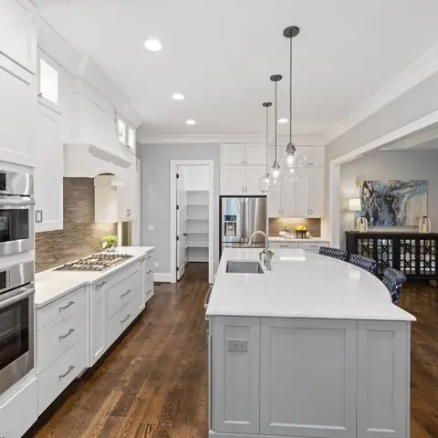 Open-plan kitchen with a white shaker island and a walk-in pantry opening onto a living room with a sofa in the same frame
