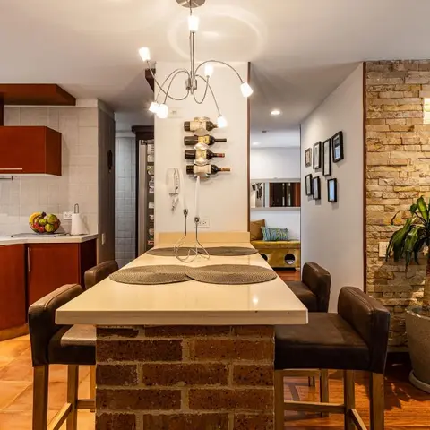Open-plan kitchen with cherry cabinetry and a brick-based breakfast bar, opening onto a living room with a stacked-stone accent wall and teal sofa