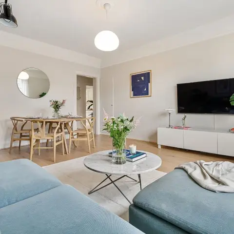 Open-plan living and dining area with a dusty-blue sectional sofa, a round marble coffee table, a wishbone-chair dining