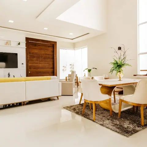 Open-plan living and dining space with a mustard-cushioned sofa beneath a floating TV shelf, a marble-top dining table on a shag rug