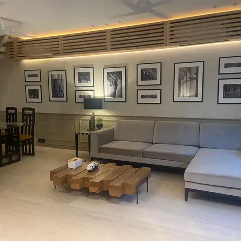 Open-plan living and dining space with a grey L-shaped sectional sofa, a chunky reclaimed-wood block coffee table, a black-and-white gallery wall