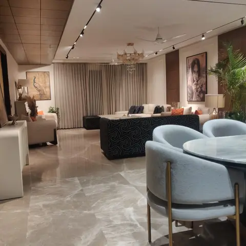 Open-plan living and dining space with a round marble dining table, powder-blue velvet chairs, a black patterned sofa and a beaded chandelier