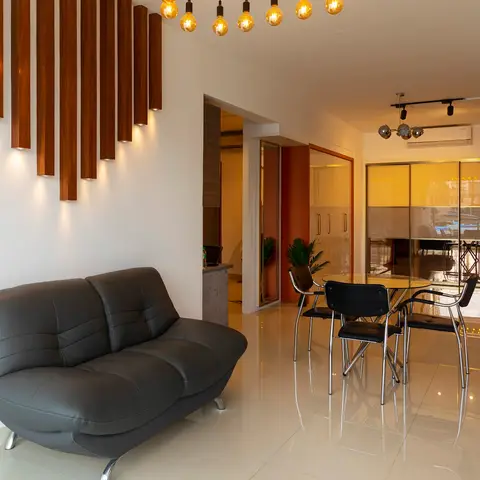 Open-plan living and dining space with a sculptural vertical wood-batten wall lit by spotlights above a grey leather loveseat