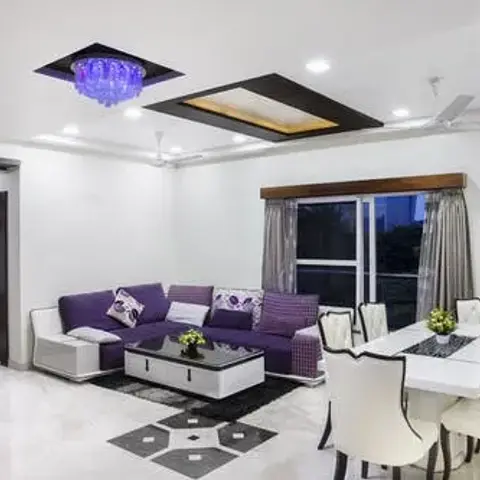 Open-plan living-and-dining space with a purple L-shaped sofa on one side and a white dining table with sculpted chairs on the other