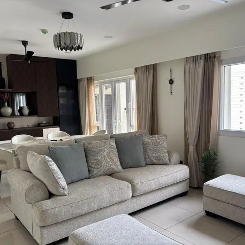 Open-plan living and dining space with a beige upholstered sofa and paisley cushions, a feather-shade pendant light, floor-length curtains