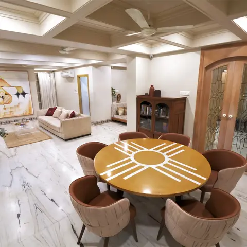 Open-plan living and dining space with a sunburst-inlay round dining table and leather barrel chairs, a cream sofa seating area, coffered ceiling