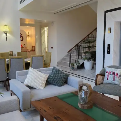 Open-plan living-and-dining space with cane armchairs, wall sconces, and a marble-clad private elevator lobby behind the sofas.