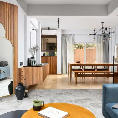 Open-plan living and dining zoned by a change from grey marble to herringbone oak, with a fluted teak wall and arched brass mirror at one end