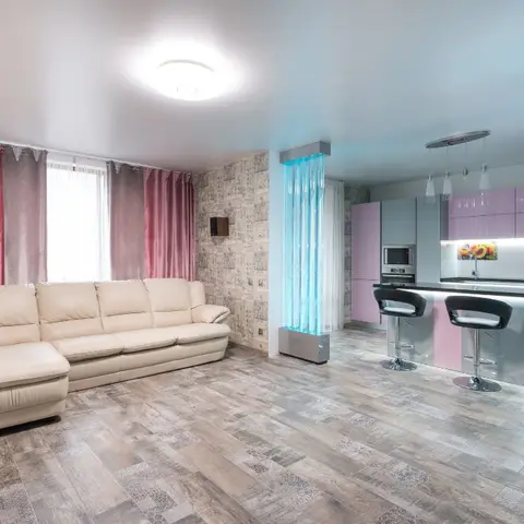 Open-plan living and kitchen with a cream leather sofa against pink satin curtains, wood-look plank flooring
