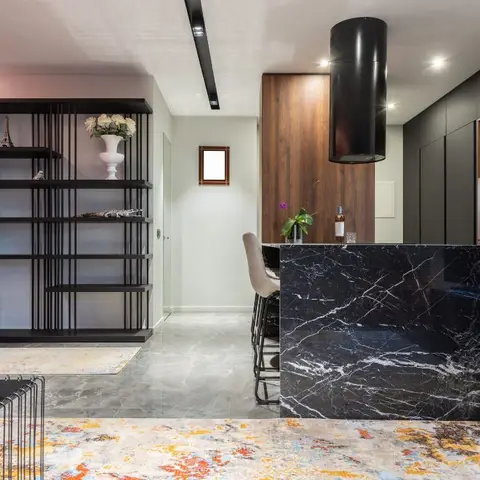 Open-plan living and kitchen with a black-marble waterfall island, cylindrical pendant light, coral fluted wall panelling and a navy sofa