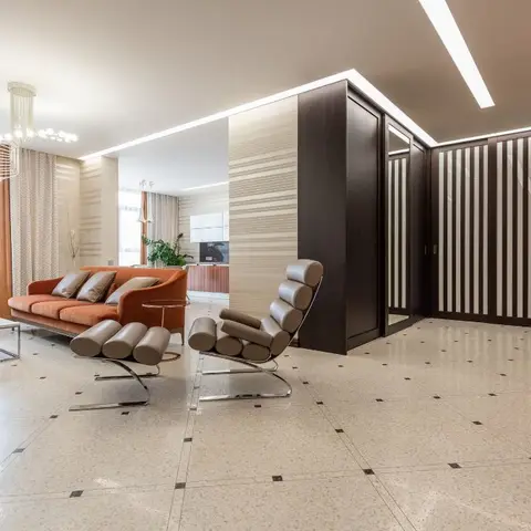 Open-plan living area with a burnt-orange curved sofa and sculptural leather lounge chairs on a terrazzo floor