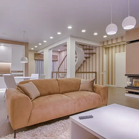 Open-plan living, dining and kitchen area with a tan suede sofa, glossy white kitchen cabinetry, a floating staircase and a built-in fireplace wall.