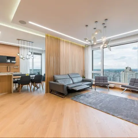 Open-plan living, dining and kitchen with a vertical wood-slat divider and floor-to-ceiling windows overlooking a city skyline.