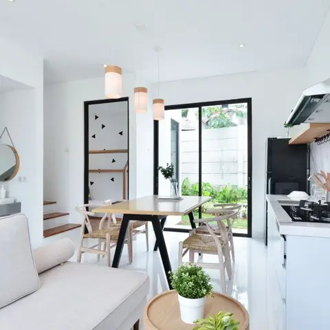 Open-plan living, dining and kitchen in white and light wood, with three pendant lights over a wishbone-chair dining table and a marble kitchen backsplash