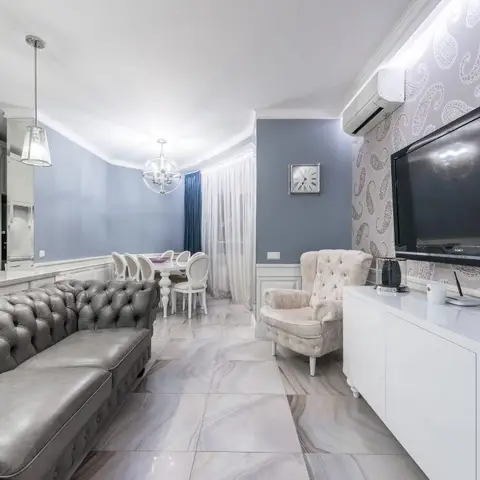 Open-plan living, dining and kitchen with a grey tufted chesterfield sofa, a grey paisley wallpaper accent wall, marble-pattern floor tiles