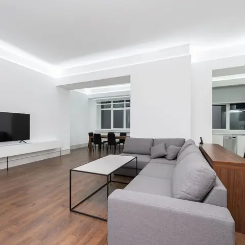Open-plan living, dining and kitchen with white cove-lit ceilings, a grey L-shaped sectional sofa, a black-frame coffee table