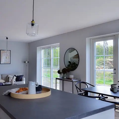 Open-plan living, dining and kitchen space with a dark stone island counter in the foreground, a round mirror and glass pendant light
