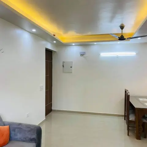 Open-plan living-dining area with a cove-lit ceiling with warm LED strip lighting, a ceiling fan, a grey sofa with an orange cushion