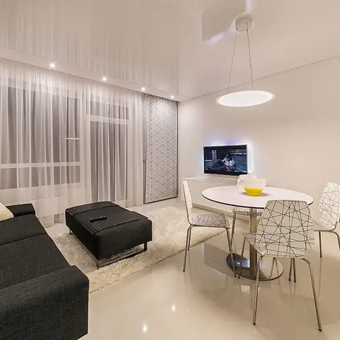Open-plan living-dining corner with a charcoal sofa and shaggy rug facing a round dining table and wire-frame chairs under a circular pendant.