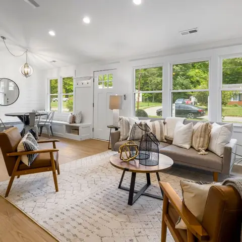 Open-plan living-dining entryway with white shiplap walls, tan leather mid-century armchairs, a round wood coffee table